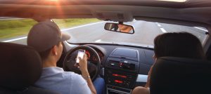 Pareja en automóvil, conduciendo por la carretera mientras el hombre visualiza su teléfono celular